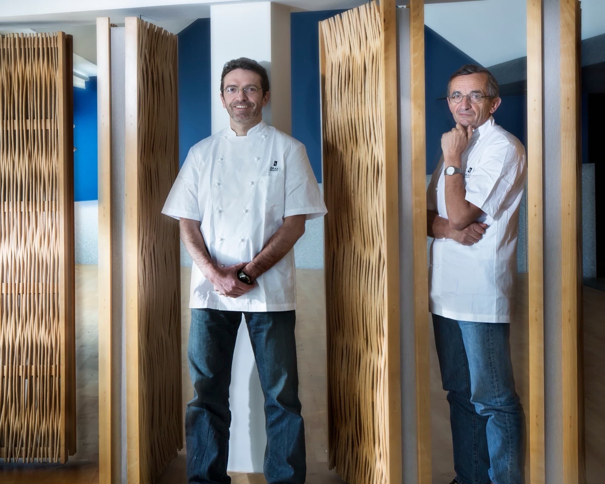 Portrait de deux chefs cuisiniers en veste blanche devant des panneaux dorés