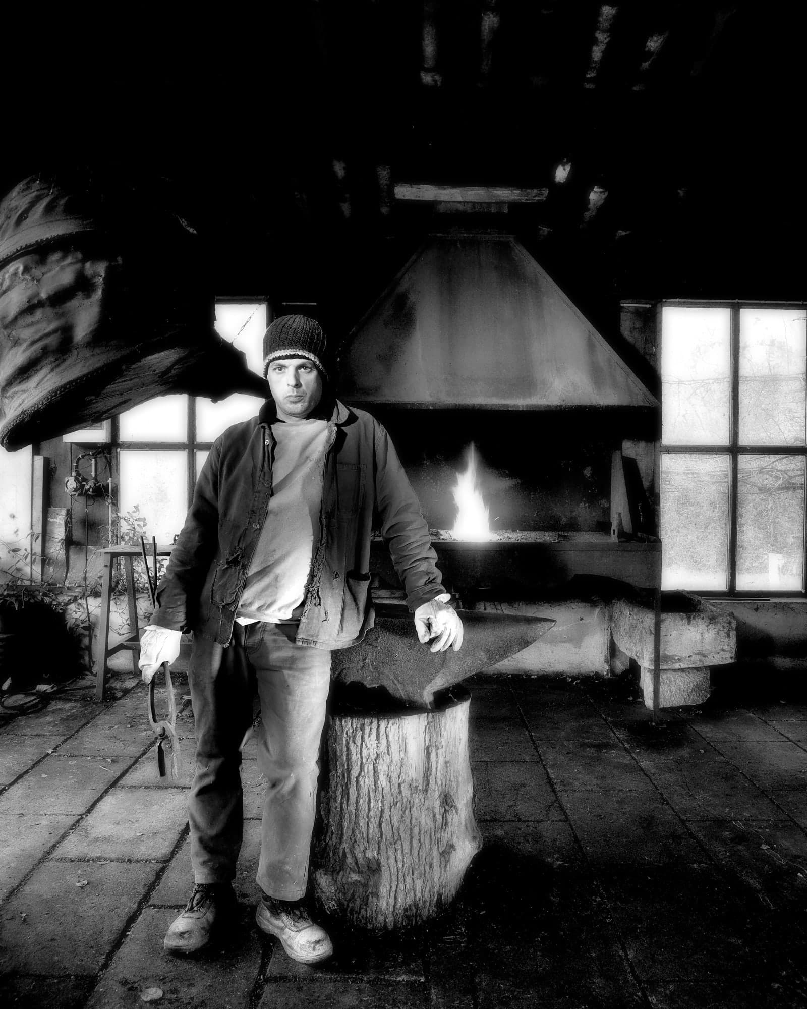 Portrait en noir et blanc d'un artisan debout devant une forge incandescente