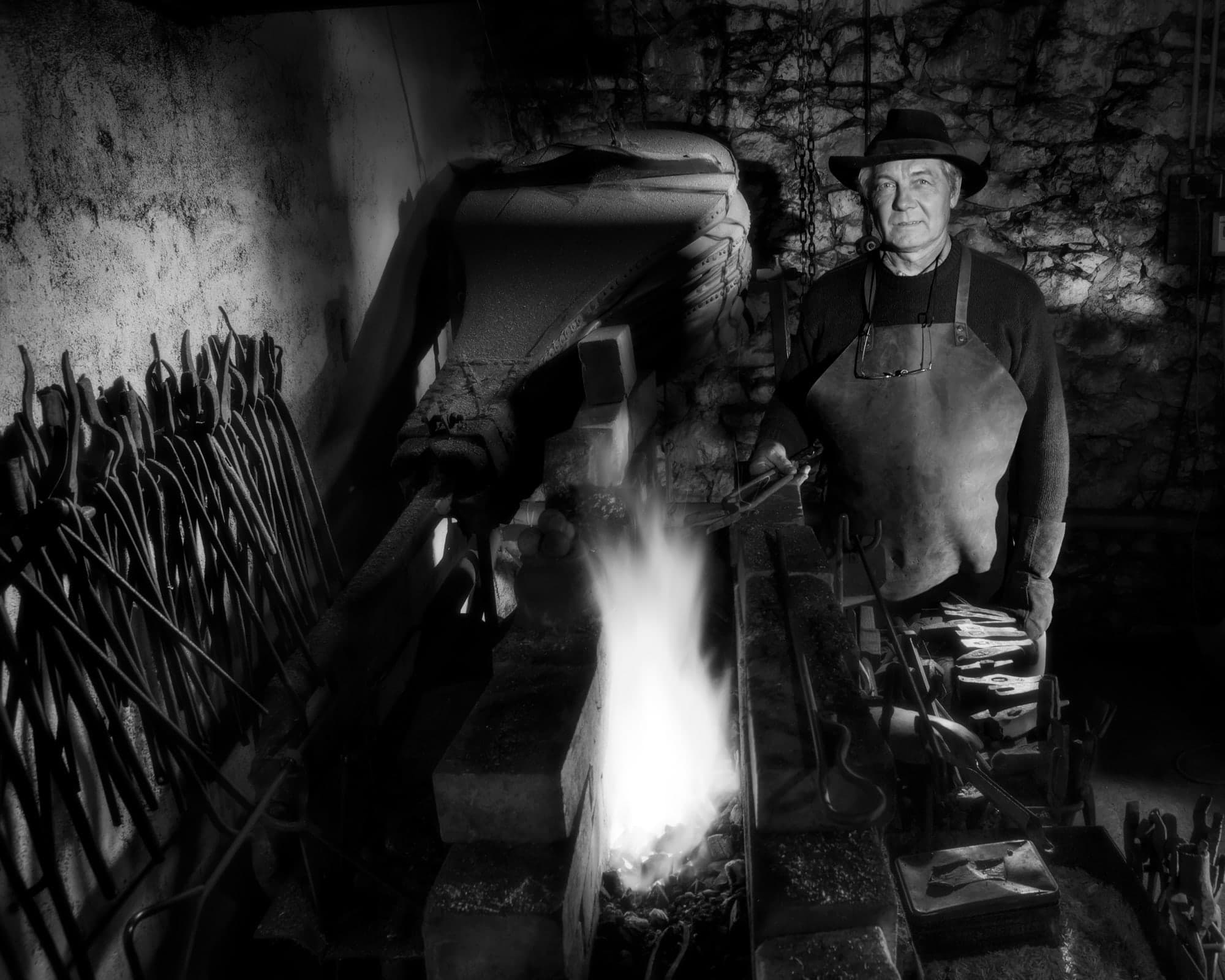 Portrait en noir et blanc d'un forgeron devant le feu de sa forge